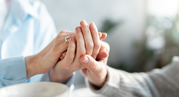 Ein jüngerer Mensch hält die Hand eines alten Menschen.
